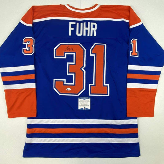Blue Edmonton Oilers hockey jersey with orange and white stripes, displaying "FUHR" and number "31" on back, flat lay view.