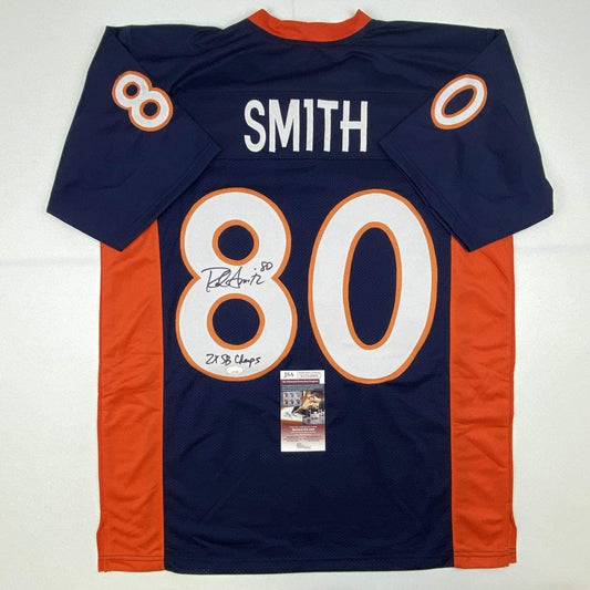 Navy blue Denver Broncos jersey number 80 with "SMITH" nameplate, signed and inscribed "2x SB Champs," displayed flat with JSA authentication certificate visible.