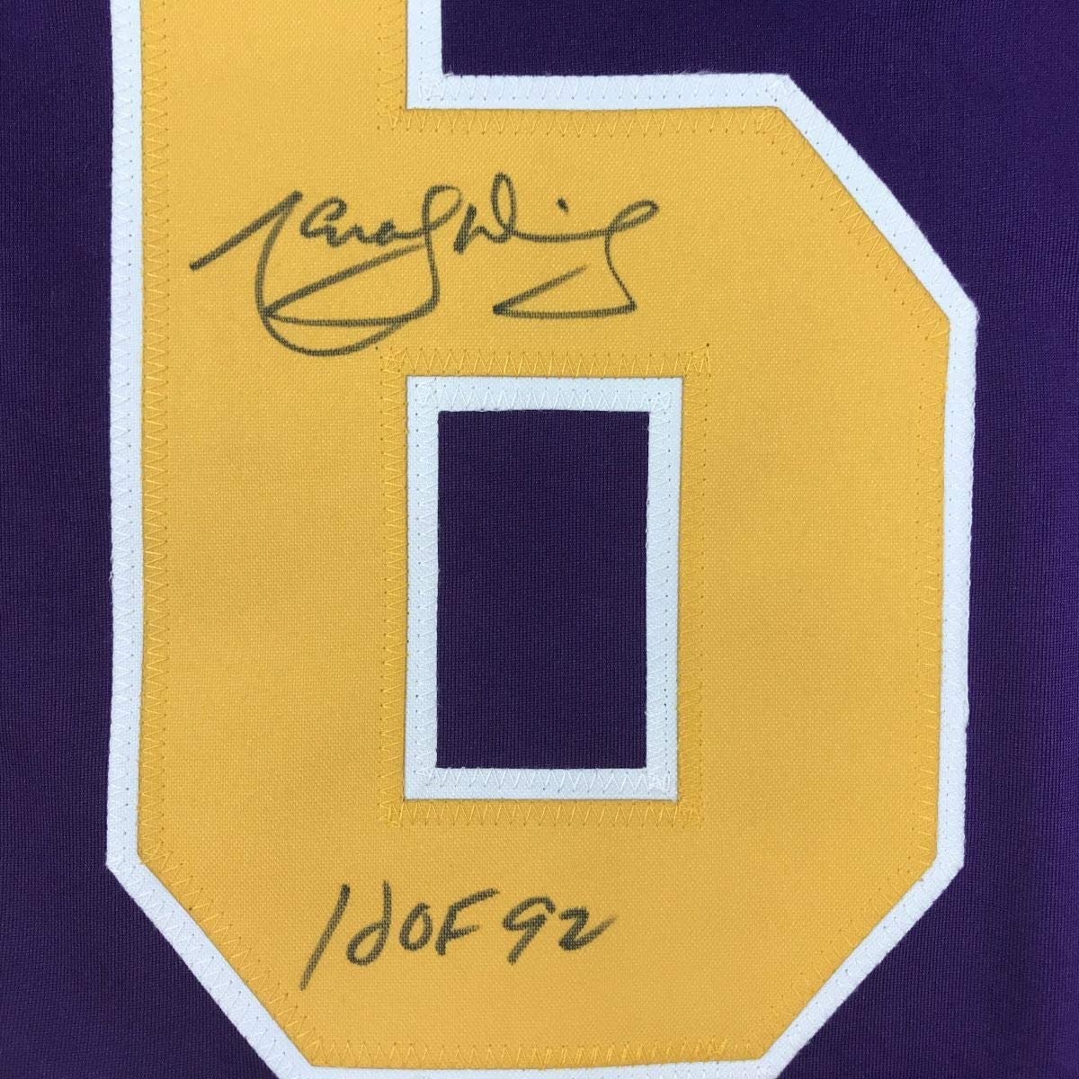 Close-up of yellow jersey patch with handwritten signature and "HOF 92" notation on purple fabric background.