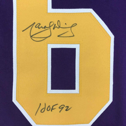 Close-up of yellow jersey patch with handwritten signature and "HOF 92" notation on purple fabric background.