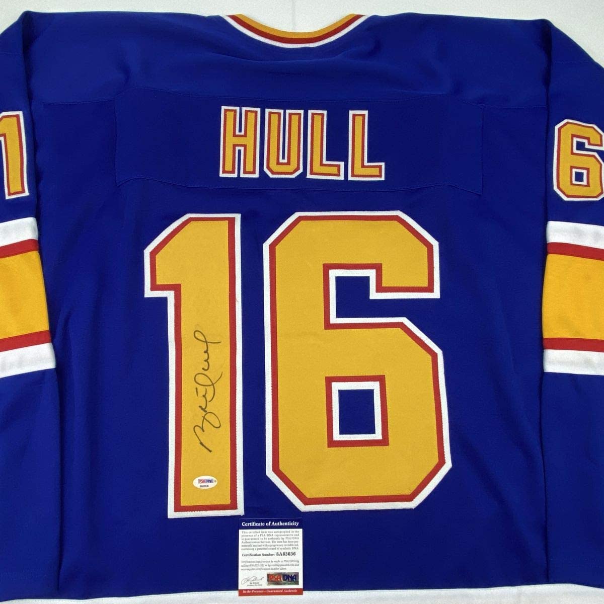 Front view of signed Brett Hull #16 St. Louis Blues retro blue jersey with yellow numbers and Certificate of Authenticity label visible.
