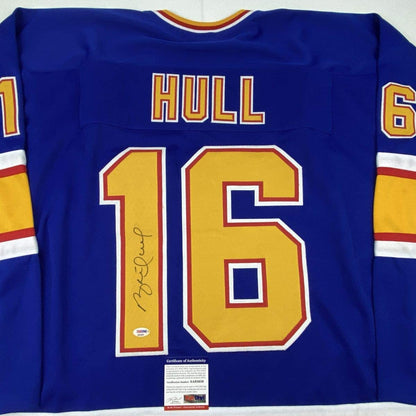 Front view of signed Brett Hull #16 St. Louis Blues retro blue jersey with yellow numbers and Certificate of Authenticity label visible.