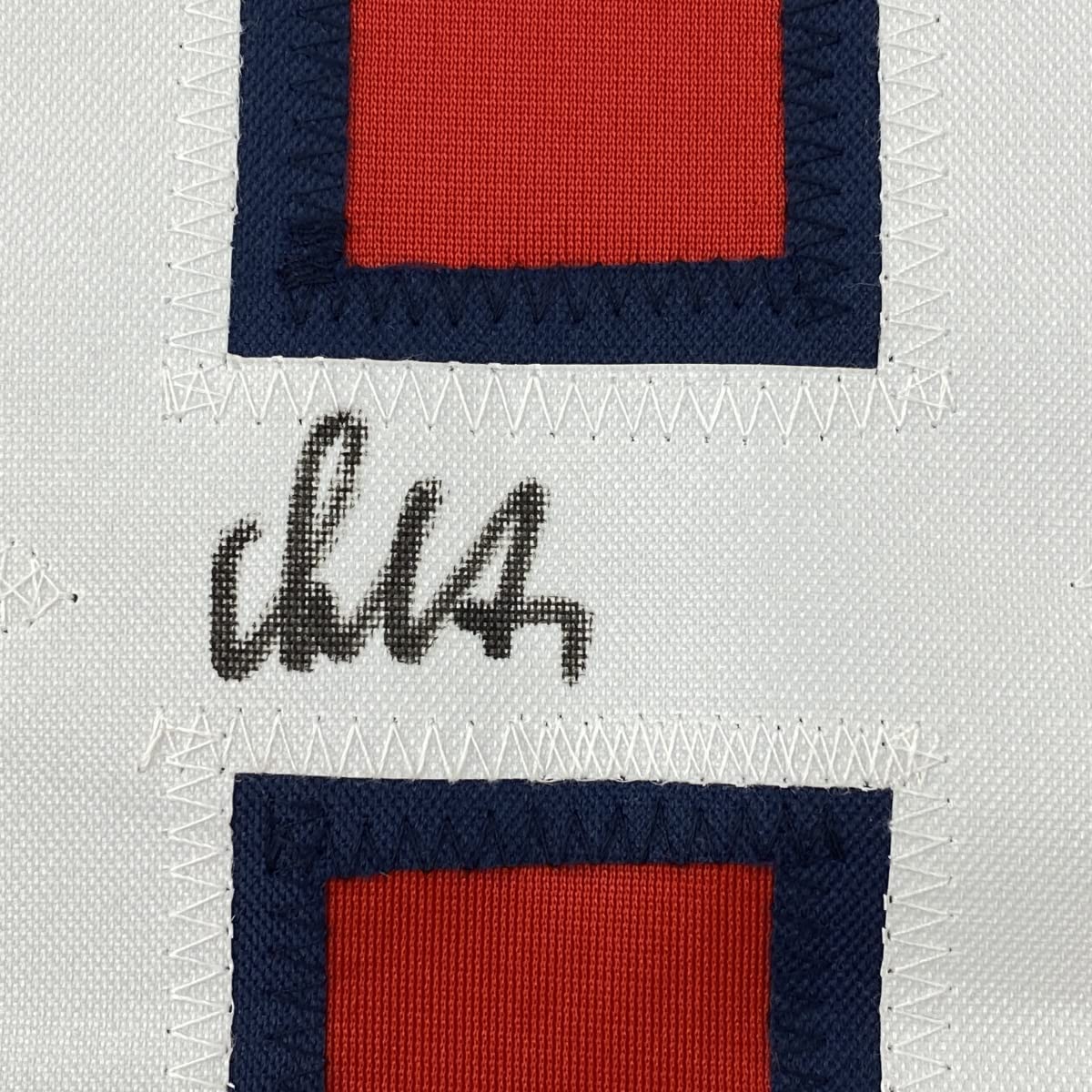 Close-up of handwritten signature on white fabric strip between two navy and red striped jersey sections.