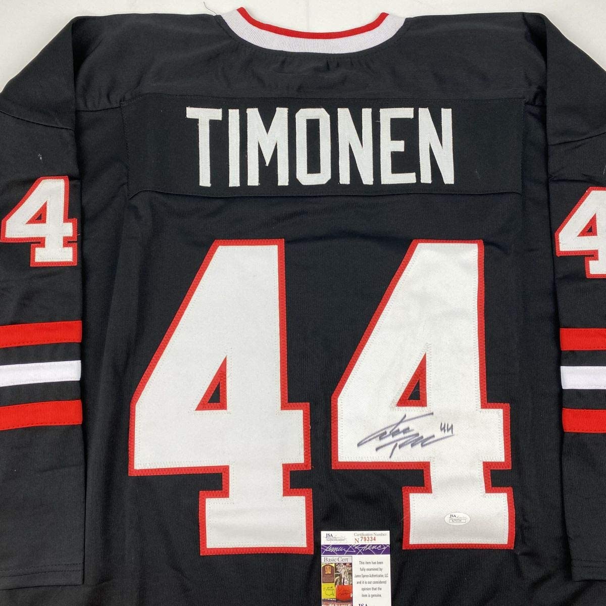 Back view of black hockey jersey numbered 44 with "TIMONEN" nameplate and red/white trim, displaying signature and JSA authentication label.