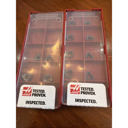Two red plastic storage cases containing carbide inserts with "TESTED. PROVEN. INSPECTED." labels on wooden surface.