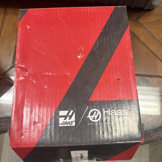 Red and black Haas F1 Team official merchandise box with diagonal stripe design and logos, overhead view on wooden floor.