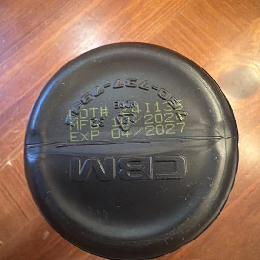 Overhead view of black plastic bottle cap with embossed "NED" logo and printed manufacturing/expiration dates on wood surface.