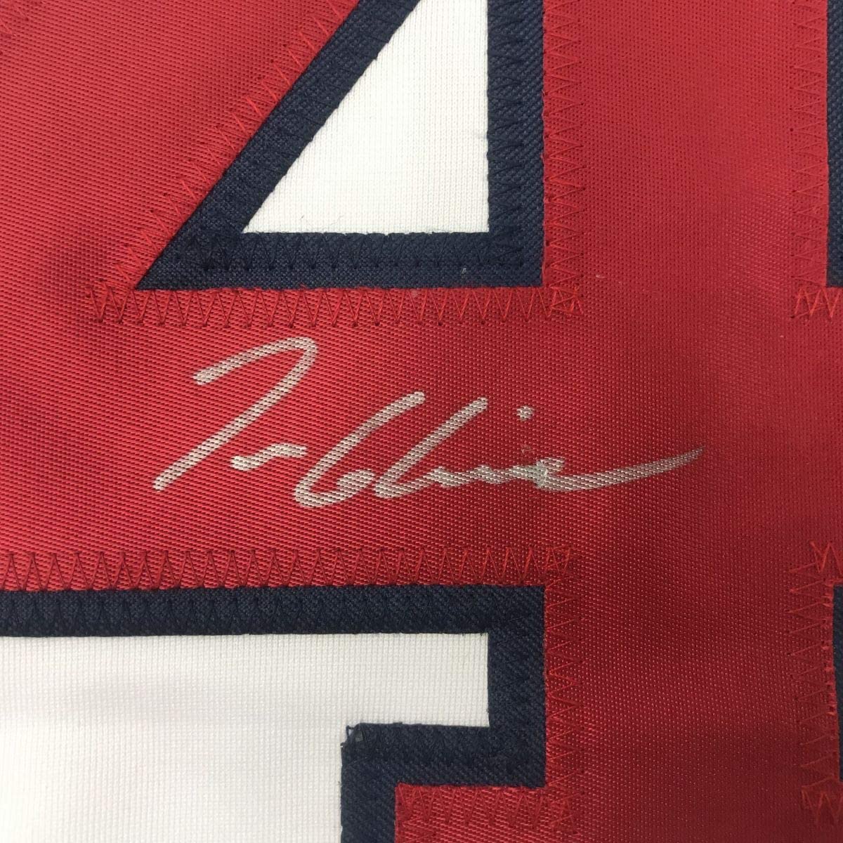 Close-up of signed red baseball jersey with navy and white striping, showing handwritten signature in silver ink.