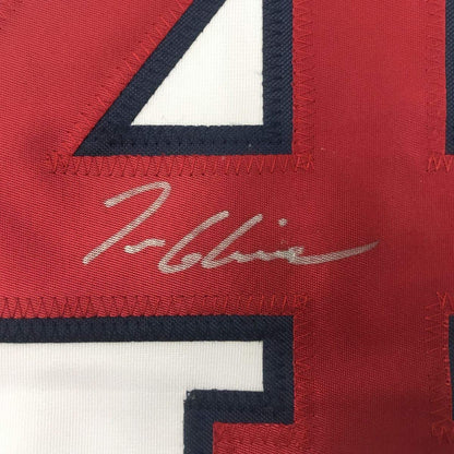 Close-up of signed red baseball jersey with navy and white striping, showing handwritten signature in silver ink.