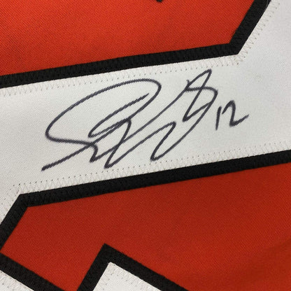 Close-up of autographed white stripe on red and black hockey jersey showing handwritten signature in dark ink.