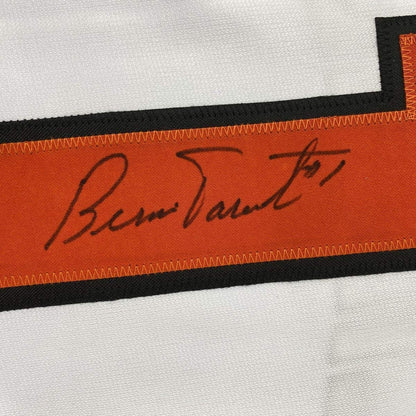 Close-up of handwritten signature "Bernie Parent" in black ink on orange and black striped ribbon trim against white fabric background.
