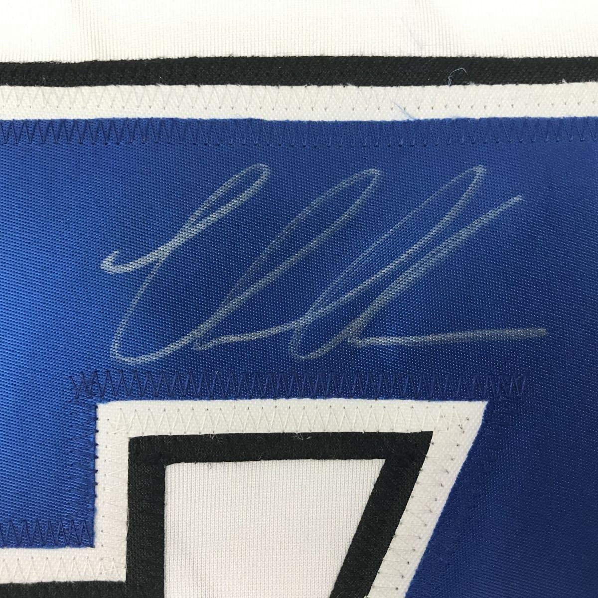 Close-up of autographed blue hockey jersey showing handwritten signature and stitched stripes in blue, white, and black.
