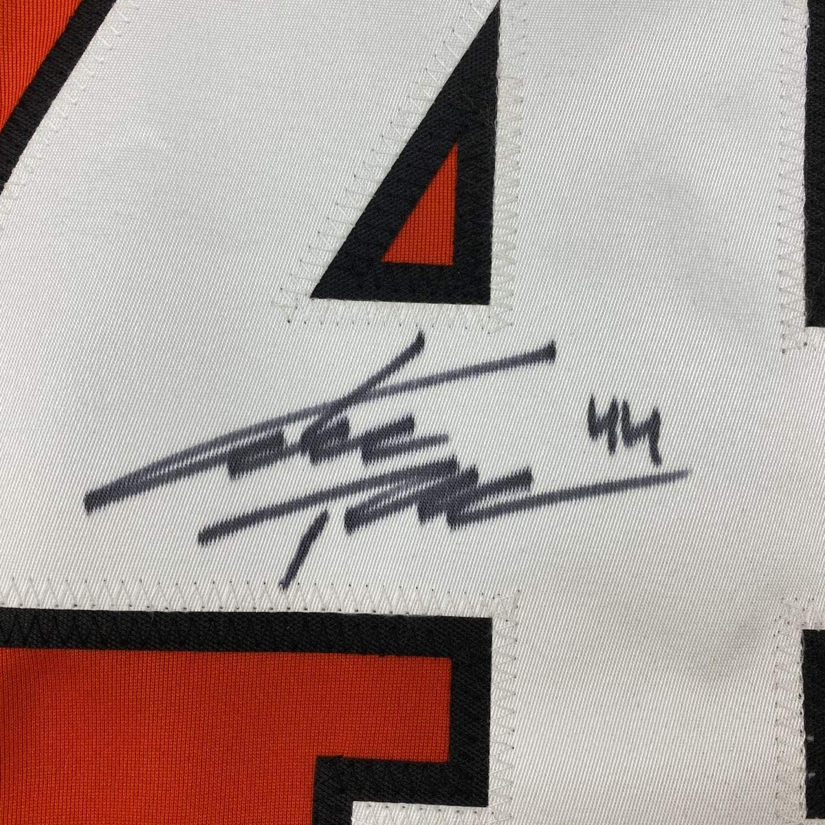 Close-up of autographed hockey jersey showing black pen signature and "44" on white fabric with red and black geometric design elements.