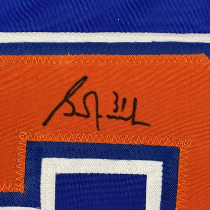 Close-up of autographed Grant Fuhr signature in black ink on orange jersey stripe with blue and white horizontal stripes visible.