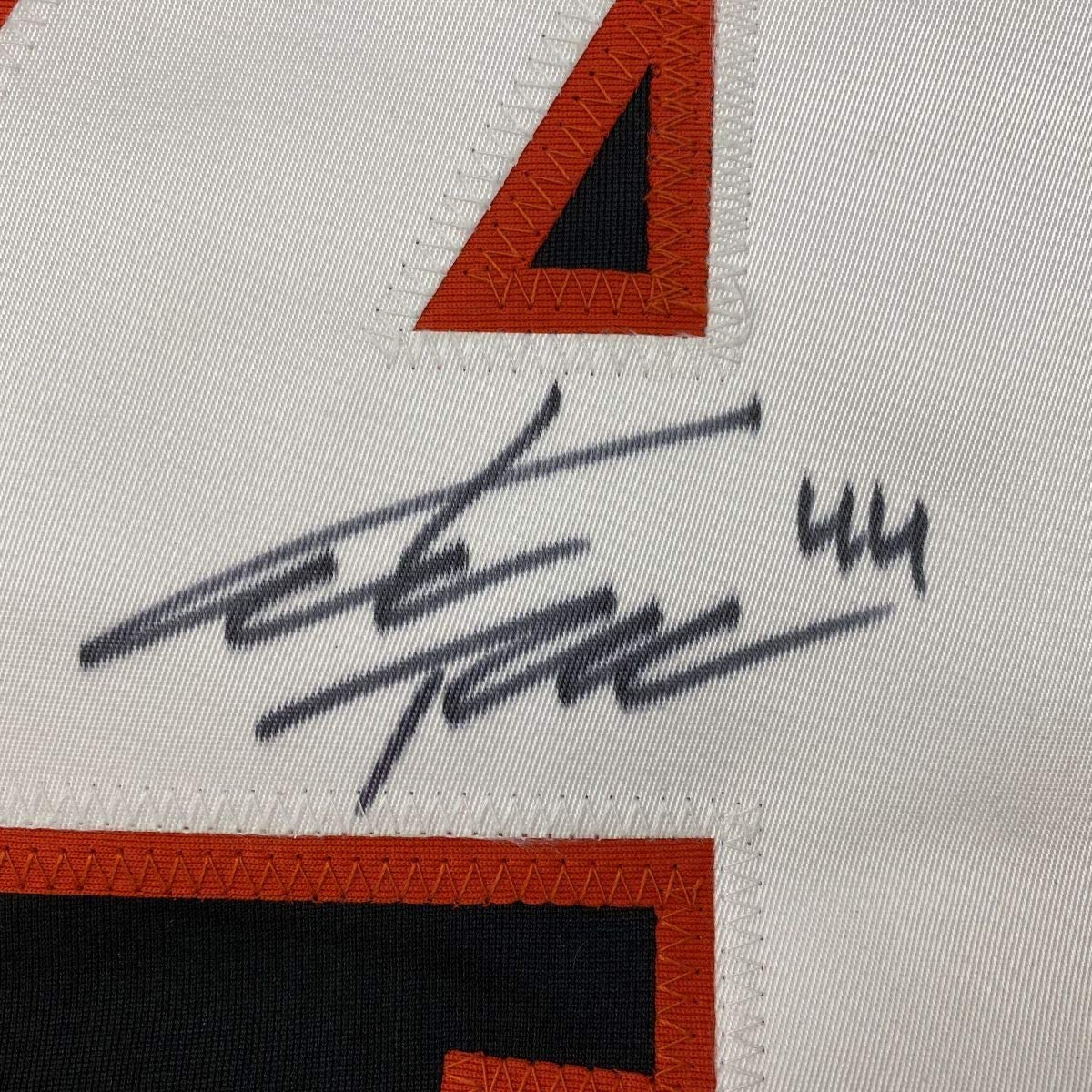 Close-up of autographed black hockey jersey with red trim showing handwritten signature and number 44 on white fabric.