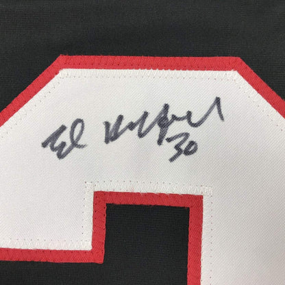 Close-up of handwritten signature on white jersey panel with red border trim.