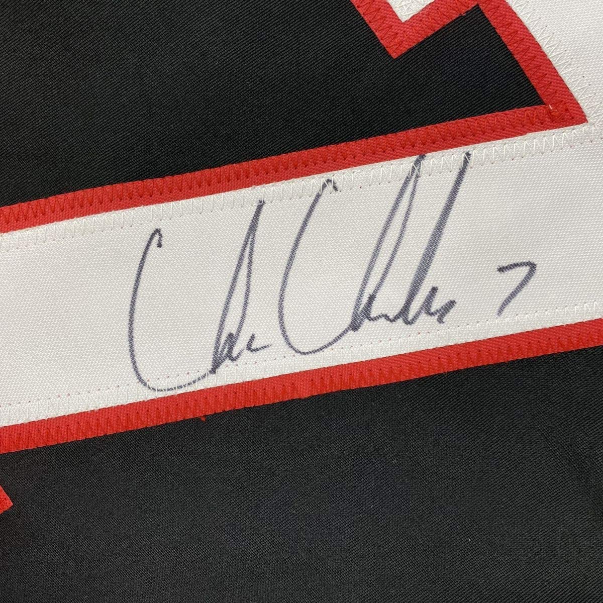 Close-up of handwritten signature on white stripe of red, white, and black hockey jersey.