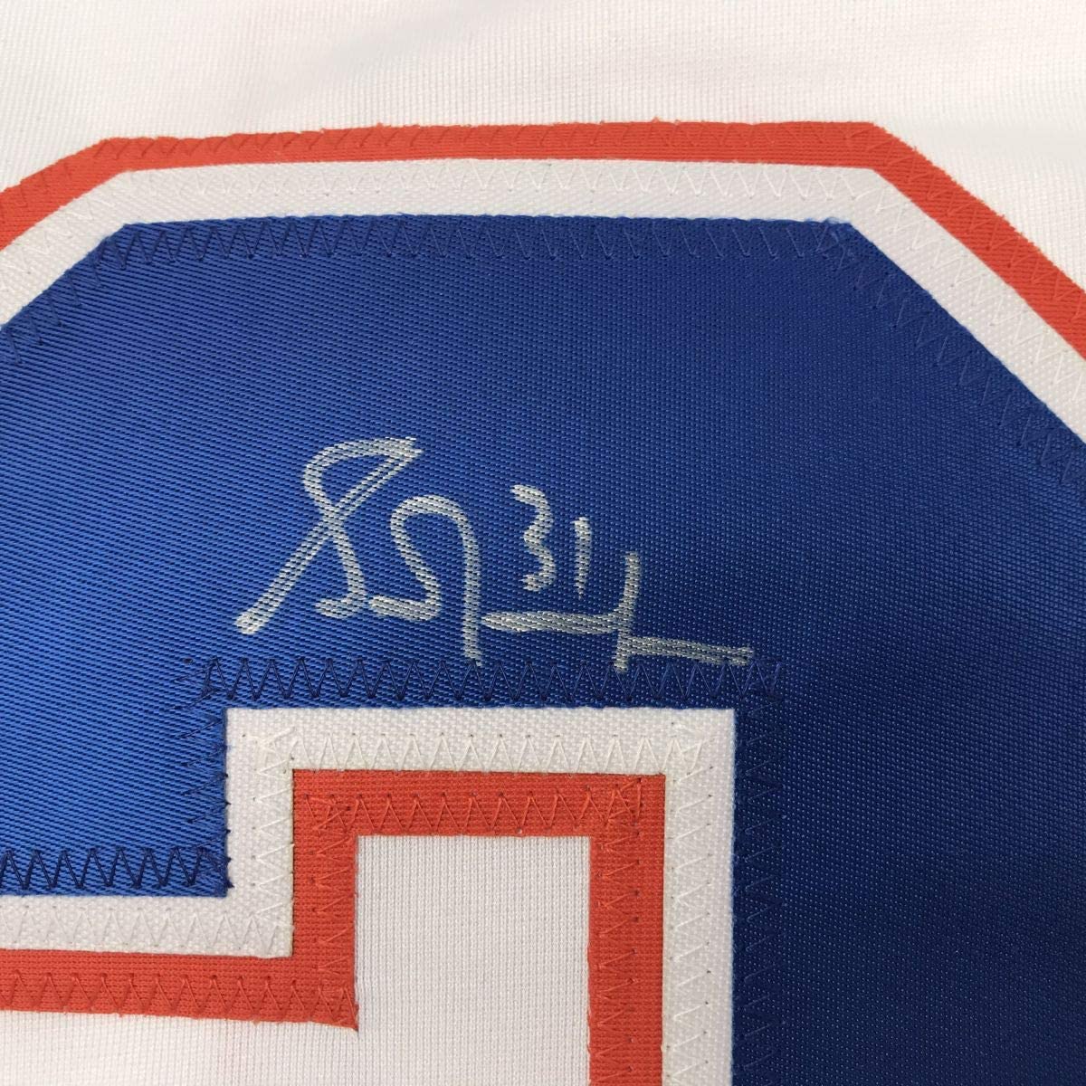 Close-up of autographed Edmonton Oilers hockey jersey showing Grant Fuhr's signature in gold ink on blue fabric with red and white striping.