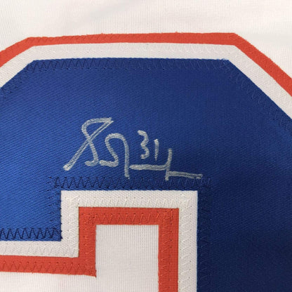 Close-up of autographed Edmonton Oilers hockey jersey showing Grant Fuhr's signature in gold ink on blue fabric with red and white striping.
