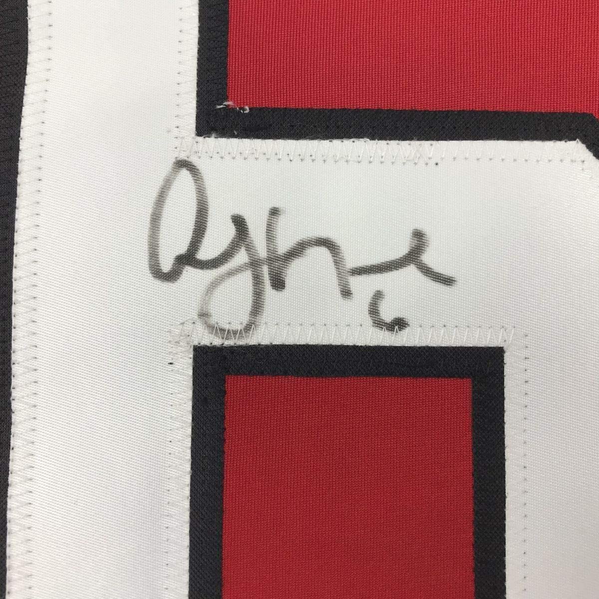 Close-up of autographed white fabric panel on red and black striped hockey jersey showing handwritten signature in dark ink.
