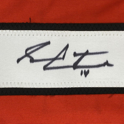 Close-up of a handwritten signature in black ink on a white fabric stripe between black and orange horizontal bands.