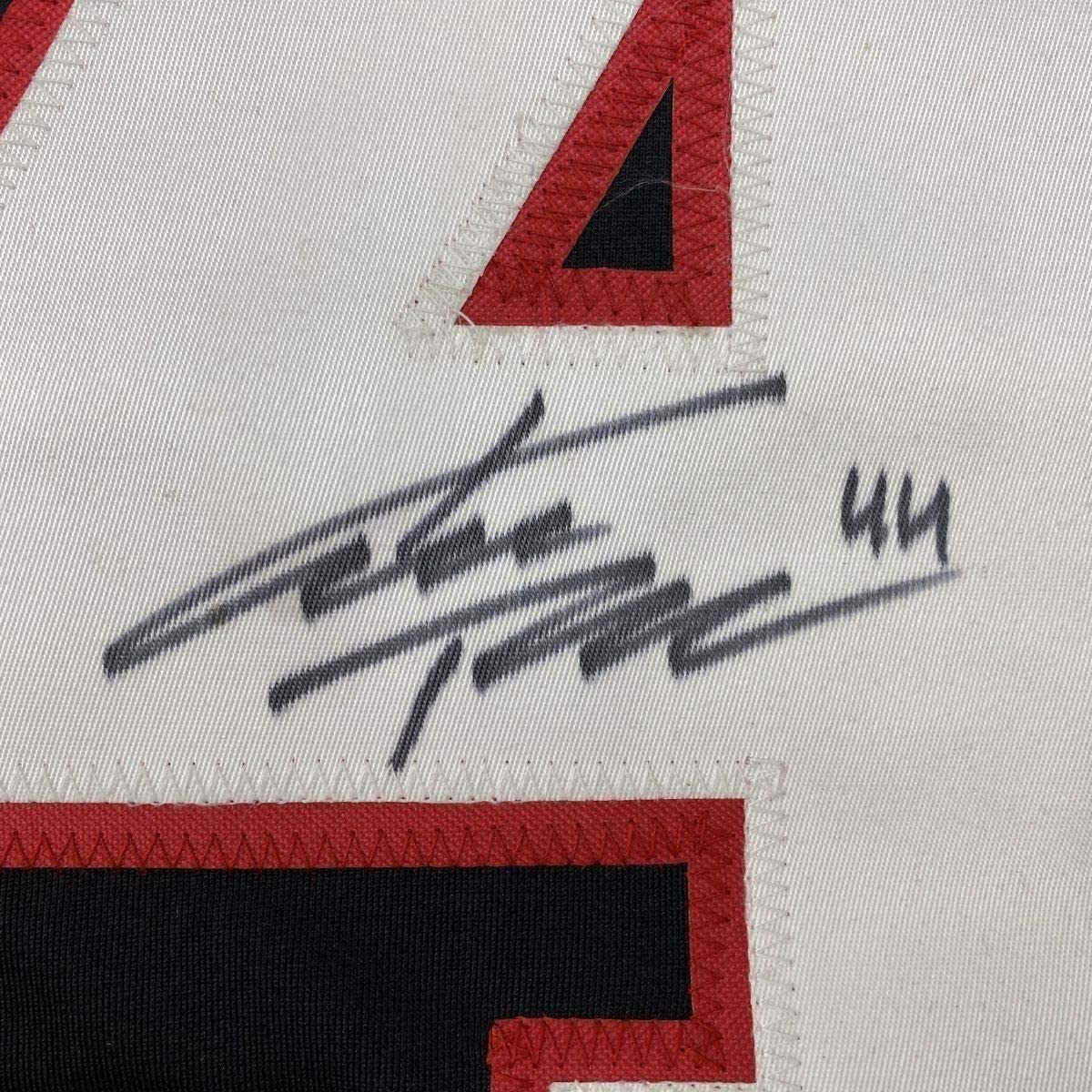 Close-up of handwritten signature in black ink on white fabric with red and black geometric design elements visible.