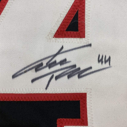 Close-up of handwritten signature in black ink on white fabric with red and black geometric design elements visible.