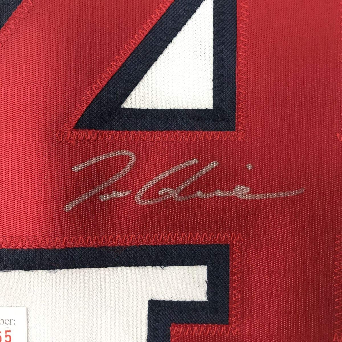 Close-up of red fabric with black and white geometric design and cursive signature in gray stitching.