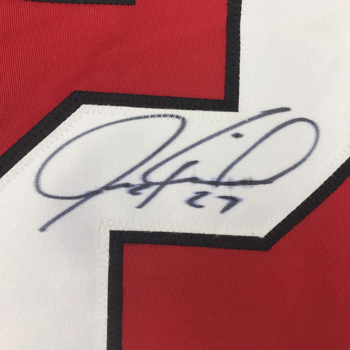 Close-up of blue handwritten signature reading "Jeremy Roenick 27" on white jersey panel with red and black fabric visible.