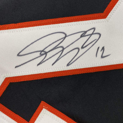 Close-up of blue handwritten signature on white stripe with red trim of black hockey jersey.