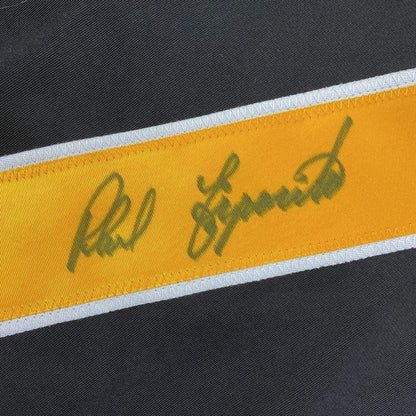 Close-up of autographed yellow and white stripe on black Boston Bruins jersey with green ink signature.
