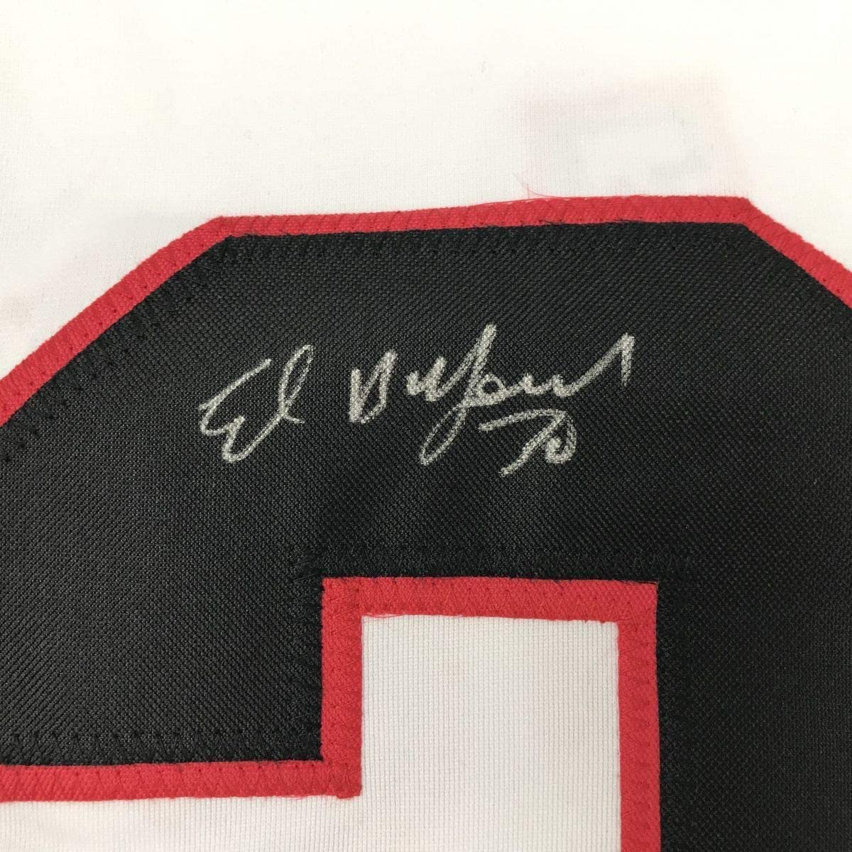 Close-up of handwritten silver signature on black fabric with red trim of hockey jersey.