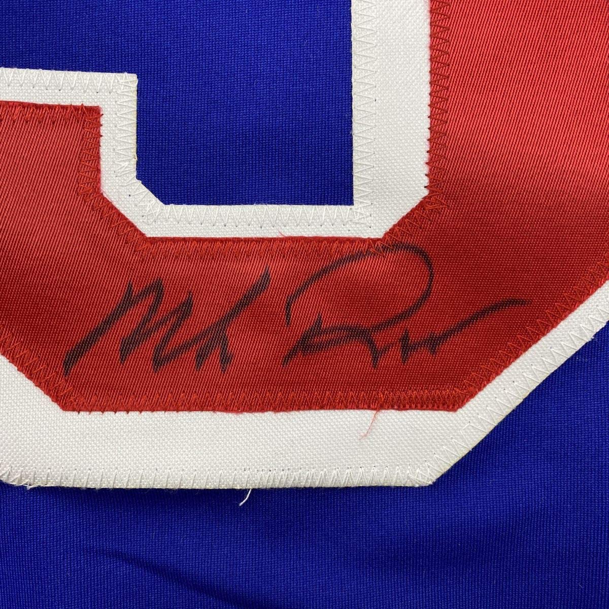 Close-up of autographed red chest stripe on blue New York Rangers hockey jersey showing handwritten signature.