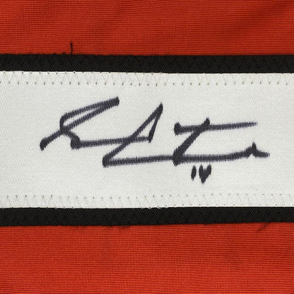 Close-up of handwritten signature on white fabric stripe between black and orange horizontal bands.
