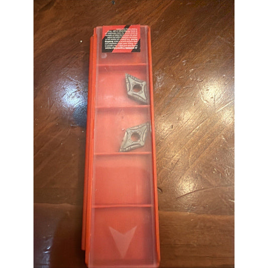 Red plastic storage case containing two metallic carbide inserts, viewed from above on wooden surface.