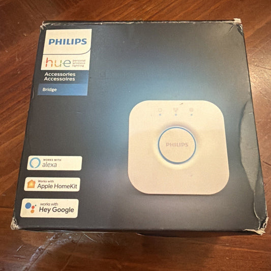 Philips Hue Bridge packaging box displayed from front angle, showing white device with blue circular button and compatibility logos for Alexa, Apple HomeKit, and Hey Google.