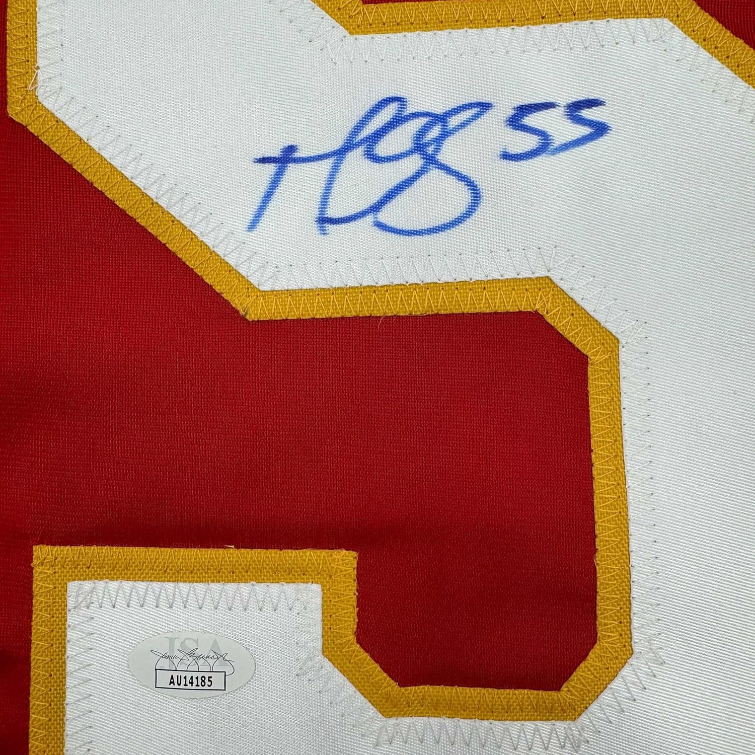 Close-up of signed Calgary Flames jersey showing blue autograph and JSA authentication sticker on white and red fabric with gold trim.