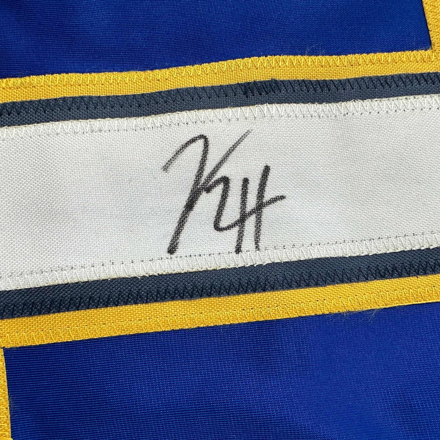 Close-up of handwritten signature on white stripe of blue, yellow, and navy striped hockey jersey.