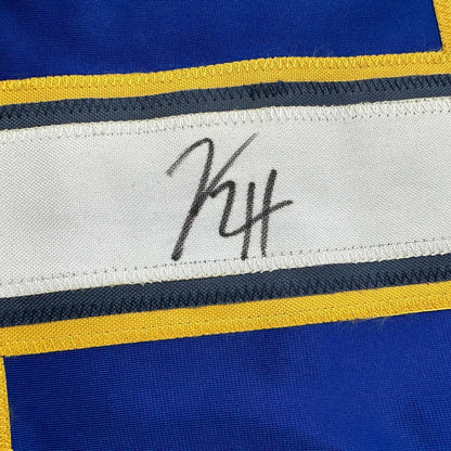 Close-up of handwritten signature on white stripe of blue, yellow, and navy striped hockey jersey.