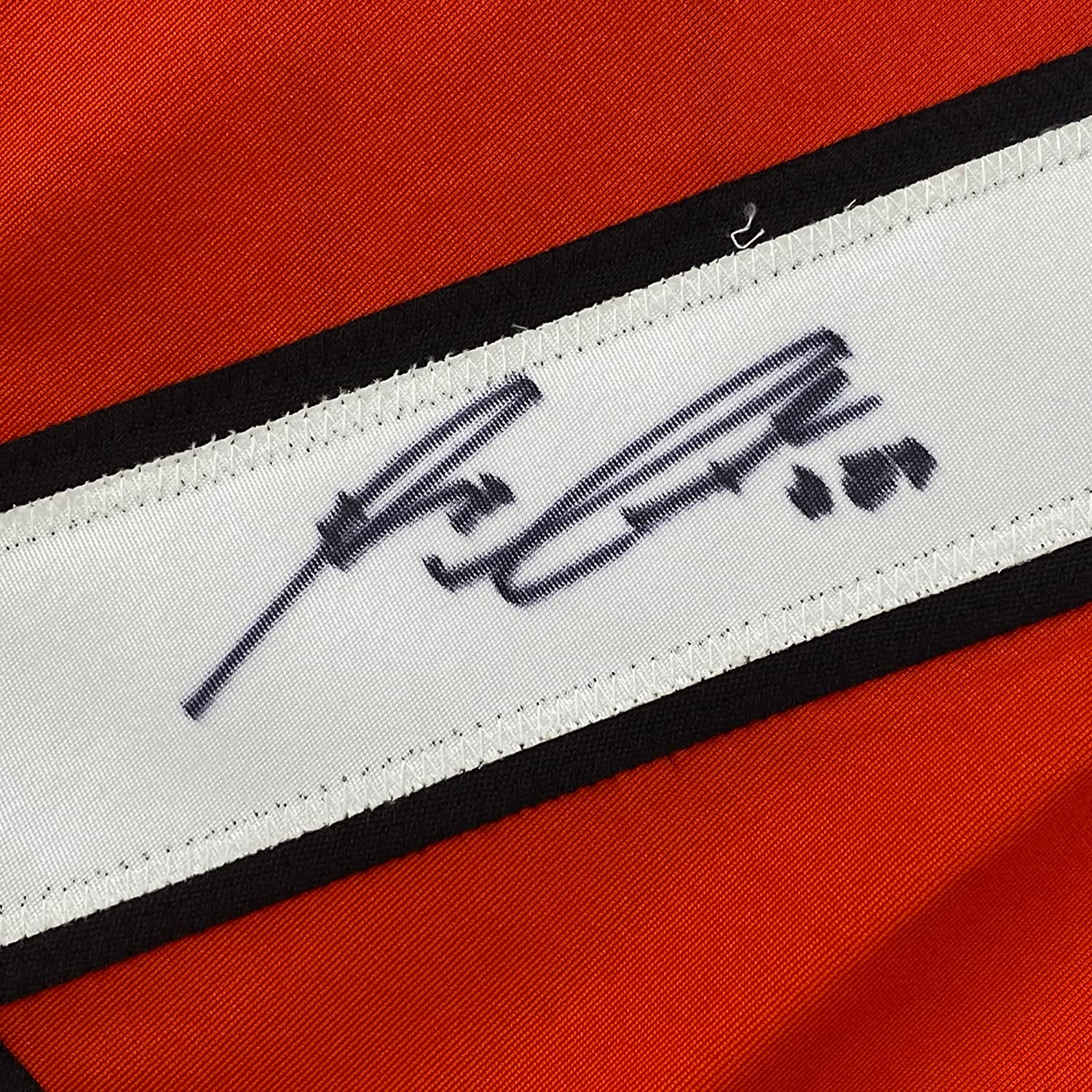 Close-up of white fabric strip with black embroidered signature on red and black striped jersey material.
