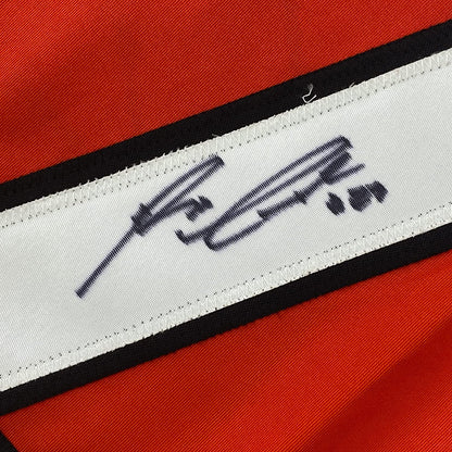 Close-up of white fabric strip with black embroidered signature on red and black striped jersey material.