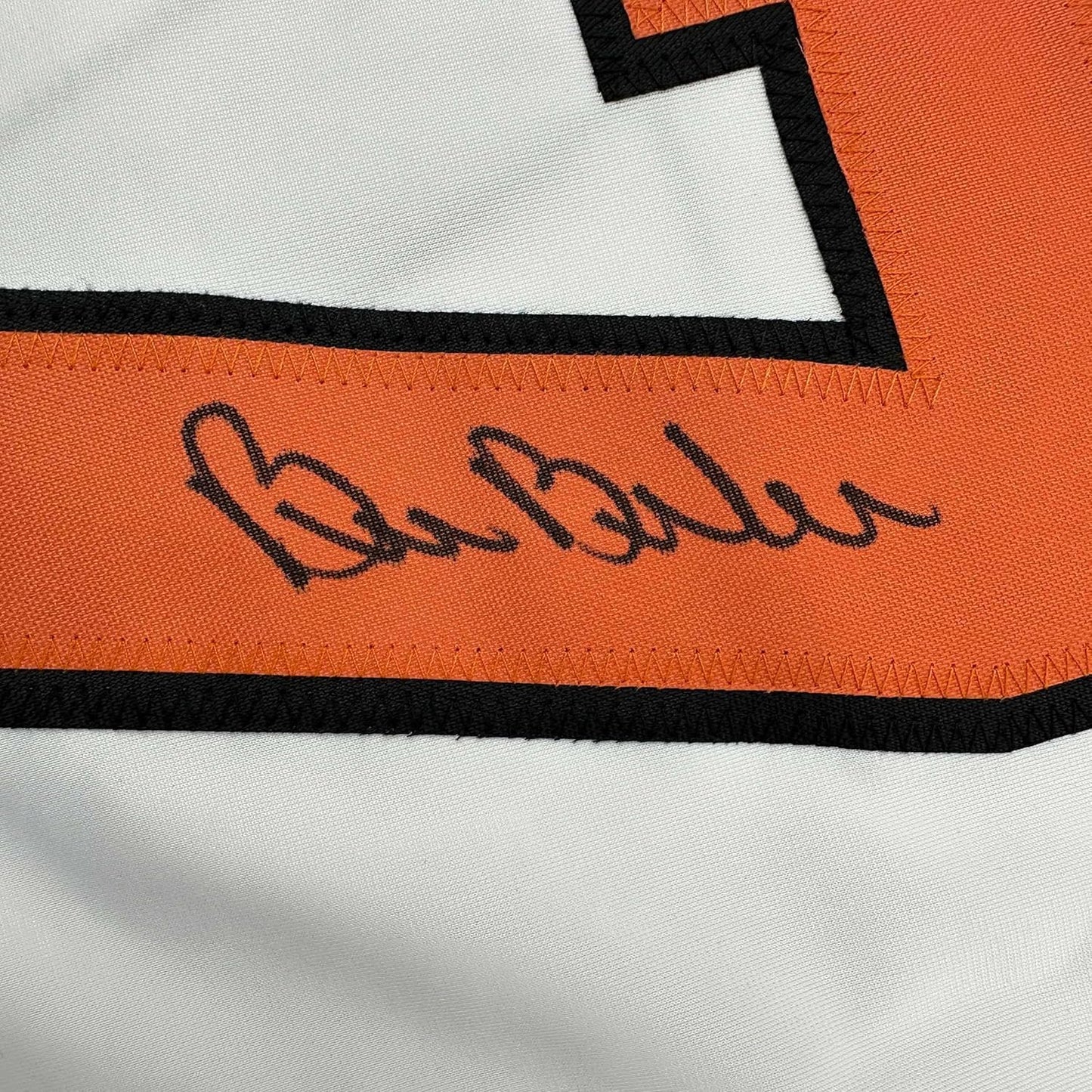 Close-up of autographed signature in dark ink on orange and white striped hockey jersey fabric with black trim.