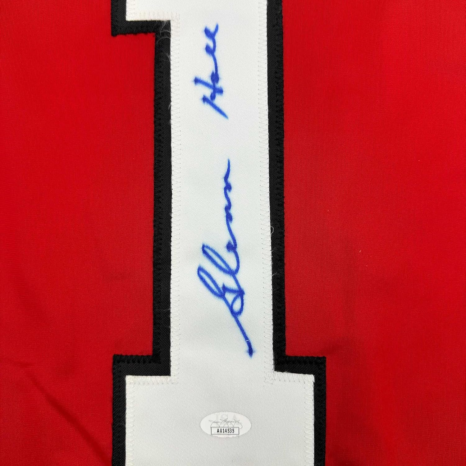Close-up of white jersey stripe with blue handwritten autograph on red Chicago Blackhawks hockey jersey.
