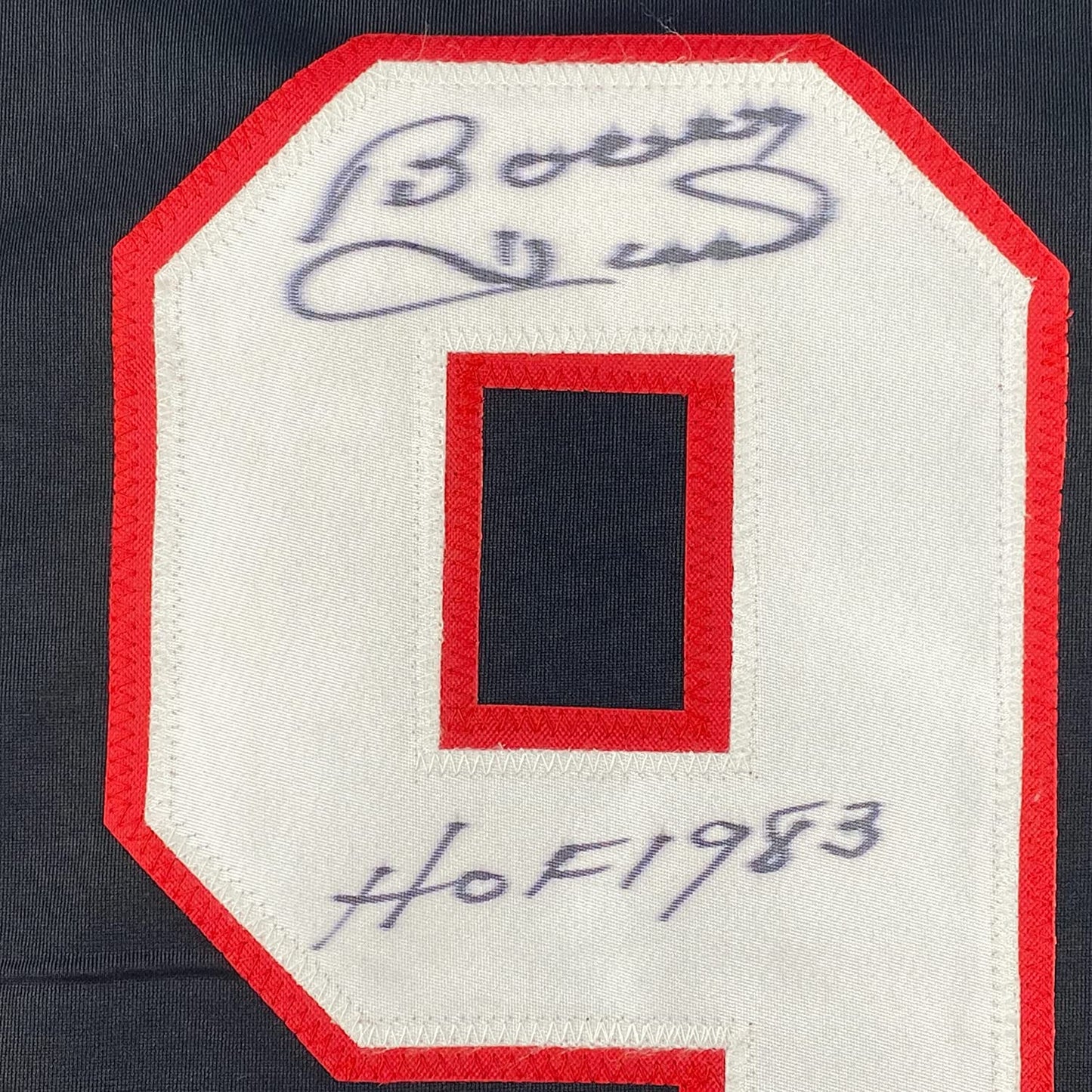 Close-up of red fabric jersey patch with handwritten blue signature and "HOF 1983" inscription on cream-colored backing.