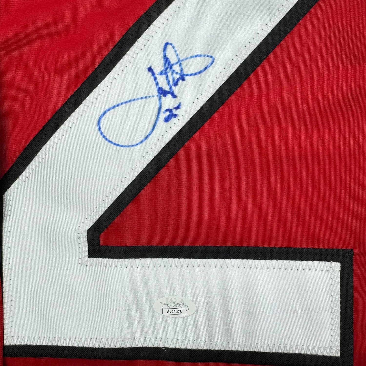 Close-up of blue autograph and JSA authentication label on white stripe with black trim of red hockey jersey.