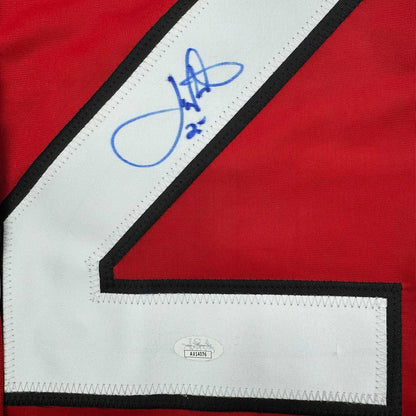 Close-up of blue autograph and JSA authentication label on white stripe with black trim of red hockey jersey.