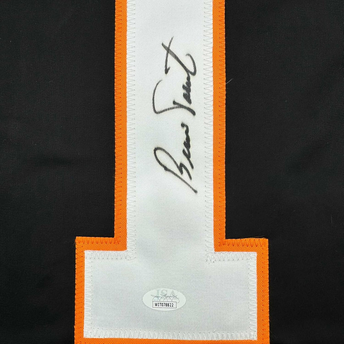 Close-up of signed white jersey panel with black handwritten signature and JSA authentication label on black and orange bordered fabric.