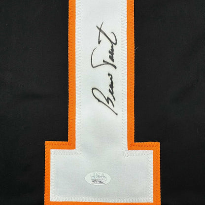 Close-up of signed white jersey panel with black handwritten signature and JSA authentication label on black and orange bordered fabric.