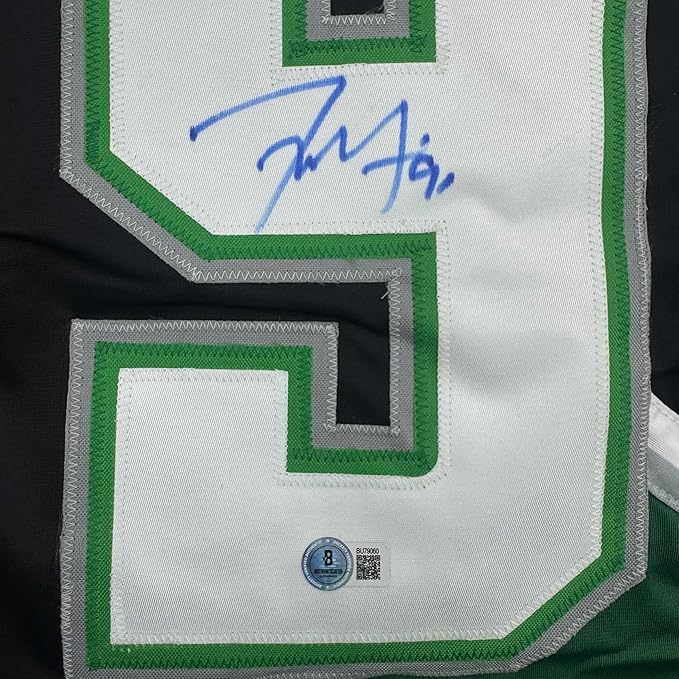 Close-up of white hockey jersey sleeve with green trim showing blue autograph signature and Beckett authentication hologram.