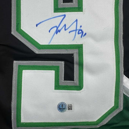 Close-up of white hockey jersey sleeve with green trim showing blue autograph signature and Beckett authentication hologram.